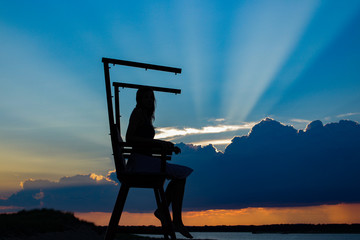 Silhouette of a woman at the beach while sitting on a lifeguard chair in sunset clouds