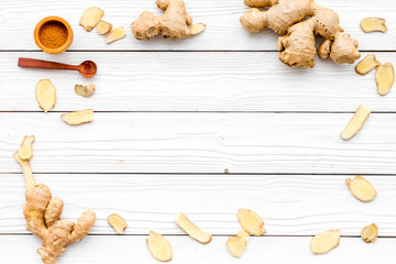 Spice and condiment. Ground ginger in small bowl near ginger root on white wooden background top view copy space