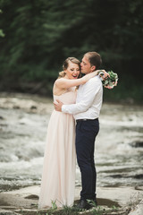 Beautifull wedding couple kissing and embracing near the shore of a mountain river with stones