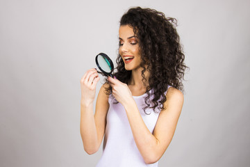 Obraz premium Beautiful girl with long curly hair and magnifier looking close up on her hair top analysing damage and dry hair concept 