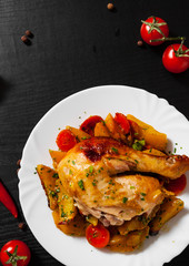 Fried chicken legs with carrots, onions and potatoes served on a white plate on dark wooden background