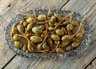 Pickled caper berries in metal dish .