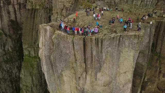 Aerial view from drone on breathtaking cliff called Preikestolen. Group of young people is standing on the edge of cliff and making the waves with hands. 4k footage, upper view. Norway.