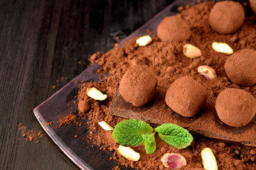 Chocolate truffles covered with cacao powder, pistachio nuts, chocolate and mint on a dark wooden board