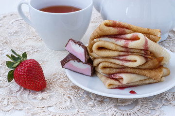 pancakes with strawberries and black tea on a white lace napkin