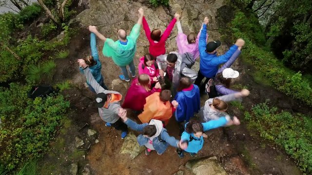 Aerial view on group of people in colorful raincoats making different figures next to the huge waterfall. 4k footage, bird view. Norway, Manafossen.