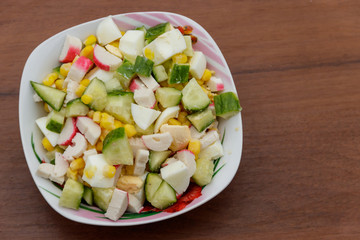 Salad with crab sticks, sweet corn, cucumber and eggs on wooden table