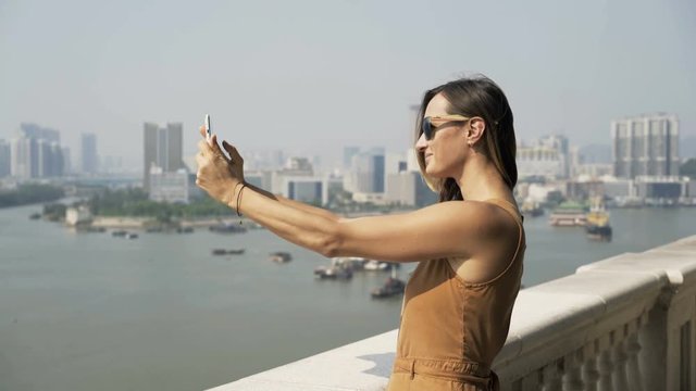 Young woman taking photos of cityscape with tablet standing on terrace in city
