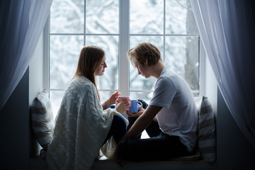 Obraz premium Young people sitting on a window-sill. They are giong to exchange their cups.