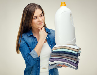 Smiling woman holding pile of clothes and detergent bottle.