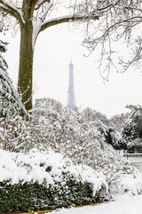 Winter in Paris in the snow. Urban landscape showing the Ajaccio park covered in snow with the Eiffel tower in the background, disappearing in the mist against a white winter sky.