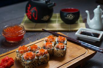 Sushi rolls served on a wooden plate in a restaurant. Sushi rolls and caviar on black wooden table. Japanese food.