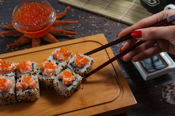Woman takes the sushi rolls using chopsticks. Black background