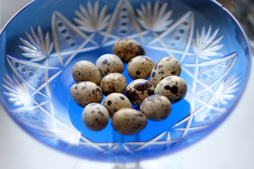 Obraz premium Spotted quail eggs in a wide crystal blue vase on a table in the kitchen
