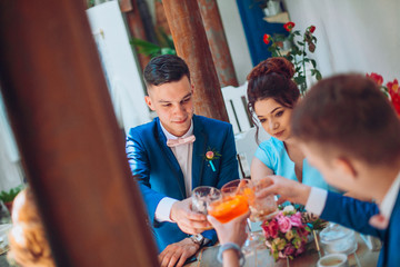 stylish happy bride and groom toasting with glasses of champagne and having fun with bridesmaids and groomsmen in cozy space cafe or restaurant. emotional moment, space for text. wedding party