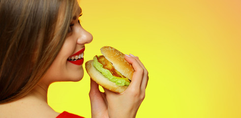 Woman with long hair holding burger standing back.