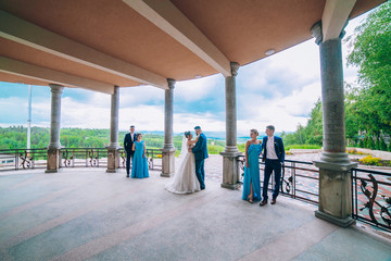 Fototapeta premium Full length portrait of newlywed couple and their friends at the wedding party. Bridesmaids and groomsman with Bride and groom near columns 