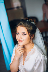 Naklejka premium Happy bride in silk robe holding her wedding dress and smiling. Wedding morning preparation.