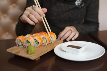 Young woman in wig eating sushi by chopsticks