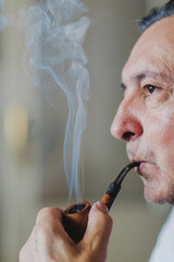 Fototapeta premium Senior man smoking a wooden pipe, releasing rich cloud of smoke