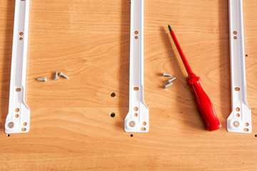 Red screwdriver lying on a wooden board. Screwing of furniture parts. Home assembling furniture.