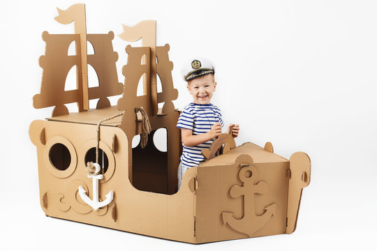 Little boy playing with cardboard ship on white background. Happy kids. Cute child dressed as a sailor. Childhood.
