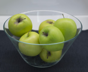glass bowl with green granny smith apples on black napkin, white background