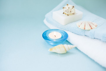 Aromatherapy spa concept with essential oil in blue glass bottle, soap bars, candle, towel and sea shells on blue background, instagram