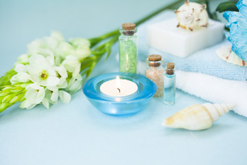 Aromatherapy spa concept with essential oil in blue glass bottle, soap bars, candle, towel, flowers and sea shells on blue background, instagram