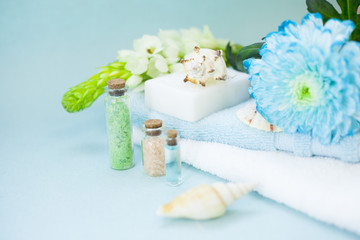 Obraz na płótnie Canvas Aromatherapy spa concept with essential oil in blue glass bottle, sea salt, soap bar, towel, flowers and sea shells on blue background, instagram