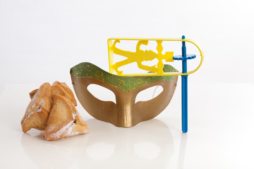 handmade green gold mask with hamantaschen Purim cookie and noisemaker on white studio background 