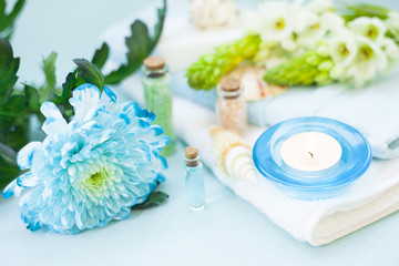 Obraz na płótnie Canvas Aromatherapy spa concept with essential oil in blue glass bottle, sea salt, towel, candle, flowers and sea shells on blue background, instagram