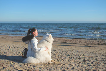 Portrait of a girl and samoyed looking into the distance on the beach. Girl and dog are resting on the beach