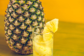 Ripe pineapple and juice in a glass on a yellow wooden background