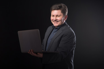 Middle aged business man with a laptop in his hands on a dark background.