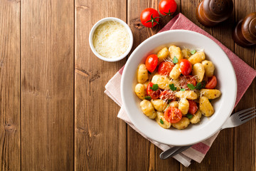 Homemade italian gnocchi with tomato, garlic, parsley and parmesan cheese on wooden table.