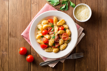 Homemade italian gnocchi with tomato, garlic, parsley and parmesan cheese on wooden table. - obrazy, fototapety, plakaty