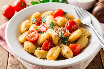 Homemade italian gnocchi with tomato, garlic, parsley and parmesan cheese on wooden table.