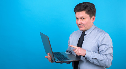 Middle aged business man with a laptop in hand on a blue background. Place for text.