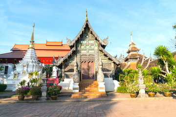 Obraz premium Ornate wooden temple facade red roof behind surrounded by plants and white chedi
