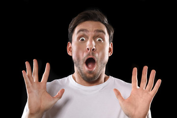 Handsome young man in a white t shirt screaming isolated on a black background. Guy shouting with his hands in the air. Stressedand scared man is yelling and cheering for his team
