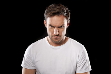 Obraz premium Angry and upset young man in a white t shirt isolated on a black background. He is in stress