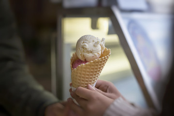 Waffle cone of two colored ice cream balls in woman's hand. Delicious cooling portion of sweet dessert on hot day and just for fun