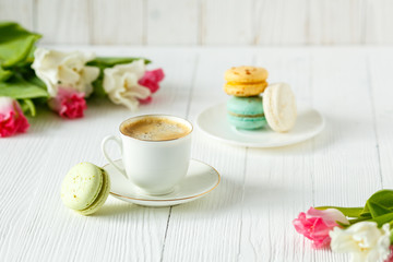 Coffee, pink and white tulips and macarons on the white wooden table