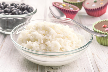 rice pudding in glass bowl on white wood with berries and other ingredients