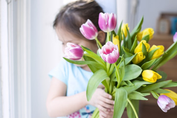 girl with a note of spring flowers. AT a cozy house in the living room by the window. Tulips of different colors. A gift on a woman's day. Card. Free space for text or a postcard.