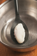 Silicone spoon, dipping a freshly pouched egg into a metal bowl of vinegar and water to prepare a breakfast dish