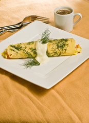 Homemade, freshly baked smoked salmon, dill crepe on a square, white plate, cup of espresso, artisan fork on a yellow cloth