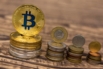  golden bitcoins lie in a pile on wooden table with usual coins