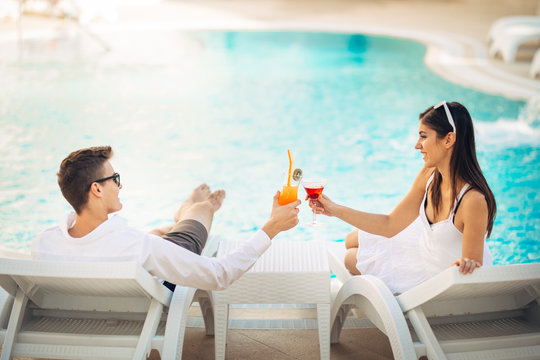 Positive happy couple having a romantic afternoon by the pool in luxury summer vacation resort.Drinking cocktails.Relaxing and enjoying spa wellness weekend.Travel, honeymoon,relationship concept